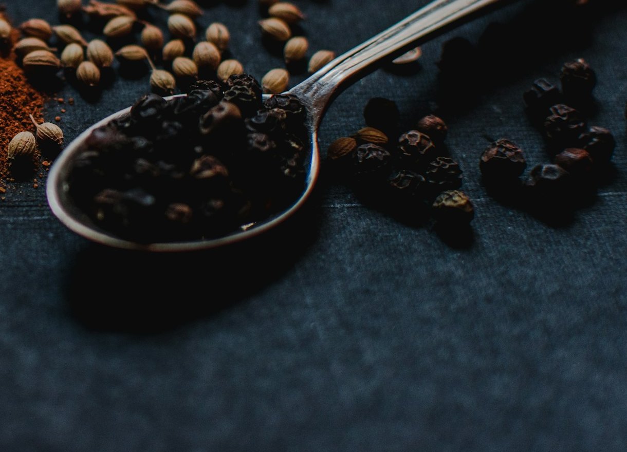 A silver spoon heaped with black peppercorns on dark slate